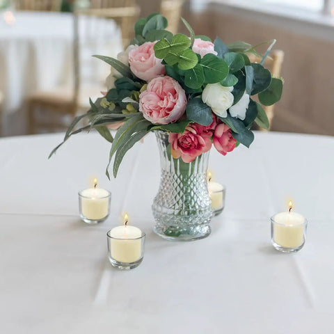 Eight-Hour Smokeless Dripless Ivory Votive Candles Bulk Pack Of 72 Sticks, displayed around flower vase on table