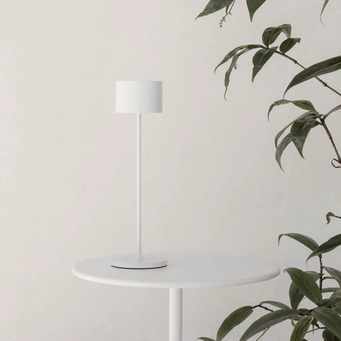 Super Sleek Portable LED Lamp In Warm Gray on round white table with green plant background. Ideal for home or desk use.