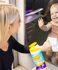 Invisible Glass Glass Wipes bottle with yellow cap; woman cleaning a glass door as a baby watches outside