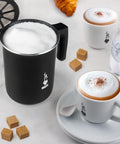 Tutto Crema Milk Frother Black Barista Grade, 1L Capacity with double fine mesh insert shown next to cappuccino cups on a table.