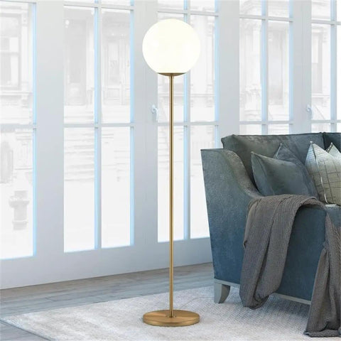 Globe And Stem Floor Lamp With Brass Finish And White Plastic Shade, Cozy Warm Glow For Living Rooms, Rock A Modern Vibe, Compatible With LED CFL And Incandescent Bulbs, Contemporary Home Lighting Solution, standing beside a blue couch in a bright room.