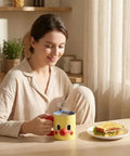 Woman holding Clown Face Ceramic Mug 10 oz yellow coffee cup with blue interior and red handle, next to breakfast