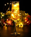 Warm White Battery Operated Fairy String Lights 10 Ft Copper Wire Set in a champagne glass with glowing effect