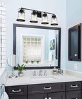 Four Light Farmhouse Vanity Lights With Rustic Wall Sconces And Hammered Glass Shades over bathroom mirror with black frame.