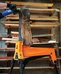Beefed Up Heavy Duty Portable Clamping Jawhorse With Foot Pedal For Hands Free Operation Folding Workbench Tripod Table 2200lb Capacity Ideal For Woodworking Repairs And Construction holding a wooden plank.