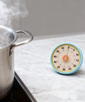 Dual Mode 60 Minute Mechanical Kitchen Timer With Magnetic Back And Built In Stand For Cooking And Baking on a marble countertop.