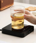 Never Suffer Through Lukewarm Coffee Again With This 20W Adjustable Mug Warmer keeping a glass of lemon drink hot on desk.