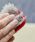 Hand using Stiff Bristle Carpet And Upholstery Scrub Brush For Auto And Home Use, Heavy Duty Grime Buster, red handle with bristles