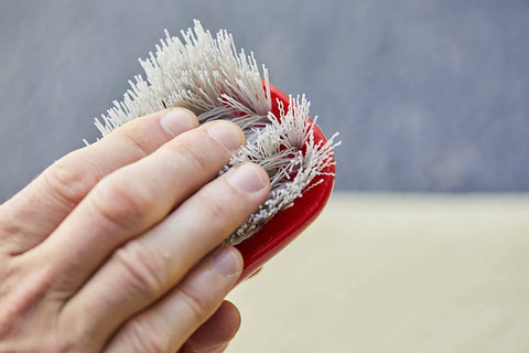 Hand using Stiff Bristle Carpet And Upholstery Scrub Brush For Auto And Home Use, Heavy Duty Grime Buster, red handle with bristles