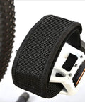 Close-up of black pedal strap on bike pedal, showcasing Two Pack Black Pedal Straps For Kids Bikes And Fixed Gear Pedals Toe Clip Style Cycling Straps Adjustable Nylon Webbing With Reinforced Stitching For Durable Foot Grip And Secure Footing On Most Bicycle Pedals.