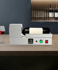 Compact Electric Heat Shrinking Machine For Pvc Bottle Sleeves And Wine Caps on a work surface with a wine bottle and glass.