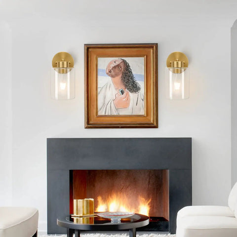 Brushed Gold Wall Sconces Set Of Two With Clear Glass Shades next to framed painting above modern fireplace.