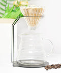 Top Shelf Iron Pour Over Coffee Dripper Rack With Rock Solid Frame Matte Black Filter Holder Stand and Precision Brewing Support For Home Cafe Kitchen Counter Setup with coffee dripper and glass carafe.
