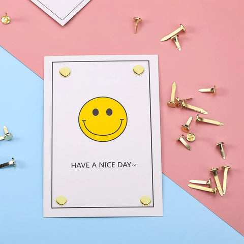 500 Piece Mini Brass Paper Fasteners Gold Pin Backs on card with smiley face, used for stationery and craft projects.