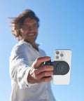 Person using SnapGrip Pro Phone Camera Grip And Magnetic Power Bank With Qi2 Wireless Charging MagSafe Compatible Shutter Button All Phones Tabletop Dock Midnight Edition.