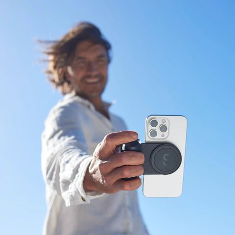 Person using SnapGrip Pro Phone Camera Grip And Magnetic Power Bank With Qi2 Wireless Charging MagSafe Compatible Shutter Button All Phones Tabletop Dock Midnight Edition.