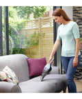 Person using Cordless Handheld Vacuum Cleaner For Home And Car With Crevice Attachment on sofa, translucent dirt bowl visible.