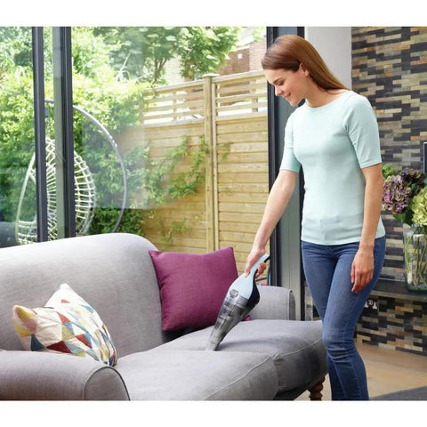 Person using Cordless Handheld Vacuum Cleaner For Home And Car With Crevice Attachment on sofa, translucent dirt bowl visible.