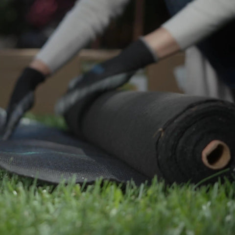 Person installing Pro Grade 5oz Landscape Fabric Weed Barrier Mat 3 Feet By 50 Feet Heavy Duty Ground Cover in garden