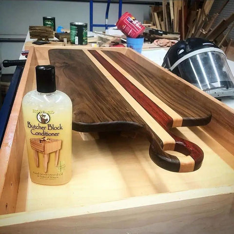 Heavy-Duty Go-To Butcher Block Conditioner And Cutting Board Oil, 12 Oz bottle next to a wooden cutting board on a workbench.