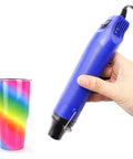 No Sweat Mini Heat Gun For Epoxy Resin And Crafts 300W Portable Handheld Dryer Tool For Embossing Shrink Wrapping Paint Clay Rubber Stamps Quick Dry Blue held next to a colorful rainbow tumbler.
