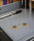 Six Pack L Shaped Brass Corner Protectors for Jewelry Boxes and Gift Boxes on a gray workshop surface
