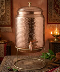 Copper Water Dispenser With Hammered Finish And Joint Free Body, Brass Stand And Tap, 5 Liter Capacity, on a table in warm decor