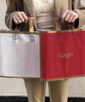 Person holding two 100 Pack Paper Gift Bags With Custom Logo For Weddings Parties And Shopping High End Hot Stamping Gray 50x45 Bottom 11cm