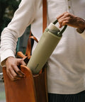 Person placing a Forty Ounce Insulated Stainless Steel Water Bottle Leakproof Travel Flask into a brown leather bag.