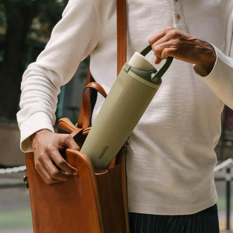 Person placing a Forty Ounce Insulated Stainless Steel Water Bottle Leakproof Travel Flask into a brown leather bag.