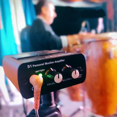 S1 Personal In-Ear Monitor Headphone Amplifier used by musician during live performance with drum set in background.