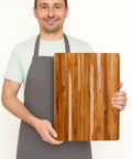Killer Size Top Shelf Teak Wood Cutting Board 20X15 Inches Food Safe Kitchen Prep Station held by a man in an apron.