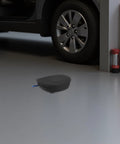 Self Activating Aerosol Car Fire Extinguisher Heat Triggered Auto Engine Bay Suppression Gear on garage floor near vehicle.