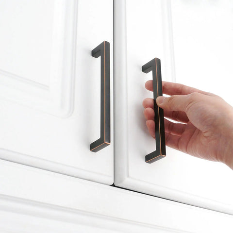 Hand holding Solid Square Oil Rubbed Bronze Cabinet Handles 5 Inch 20 Pack For Kitchen Cabinets Drawers Dresser Cupboard Bedroom Bathroom Hardware Built To Last With Smooth Edges And Easy Install Dope Look on white cabinet doors