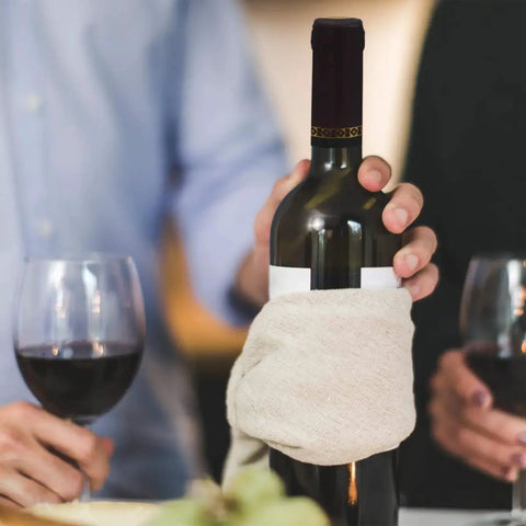 Person holding wine bottle with Pro Grade PVC Heat Shrink Capsules For Wine Bottles 100 Pack Black Sealer Shrink Caps, glasses nearby.