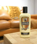 Leather Conditioner With Deep Nourishing Moisturizers And Natural Waxes To Restore Dried Leather To A Soft Natural Feel Without Oiliness Or Stickiness 8 Ounce Bottle For Boots Belts And Leather Goods on a wooden table with a leather couch in the background.