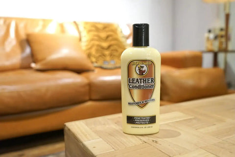 Leather Conditioner With Deep Nourishing Moisturizers And Natural Waxes To Restore Dried Leather To A Soft Natural Feel Without Oiliness Or Stickiness 8 Ounce Bottle For Boots Belts And Leather Goods on a wooden table with a leather couch in the background.