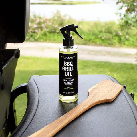 Plant Based BBQ Grill Cleaner Oil For Grates And Grills 8 oz bottle on grill with wooden scraper in outdoor setting