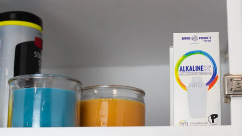 Alkaline Water Pitcher Replacement Cartridges Three Pack 80 Gallon Life Per Cartridge box on shelf near candles.