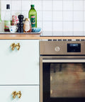 Gold Bow Cabinet Knobs Set Two Pack Brass Finish Bow Shaped Pulls on Kitchen Cabinets Next to Stainless Steel Oven