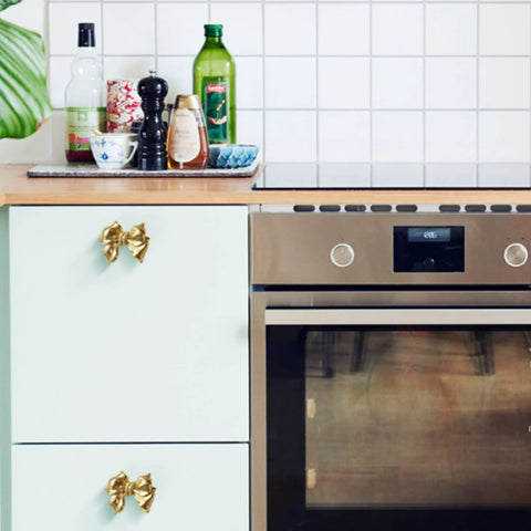 Gold Bow Cabinet Knobs Set Two Pack Brass Finish Bow Shaped Pulls on Kitchen Cabinets Next to Stainless Steel Oven