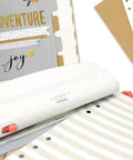 Adjustable Six Hole Punch for Pocket Journals and Planners, 8 Sheet Capacity, shown on a desk with punched paper and planners