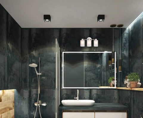 Bathroom interior with metallic finish and frosted glass three-light fixture above mirror, modern minimalist design.