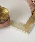 Pebeo gilding wax King Gold jar; angled top-down view of a white frame corner being gilded with gold wax and cloth