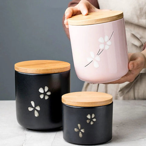 Matte Black Ceramic Coffee Canister With Premium Airtight Seal Keeps Your Daily Grind Fresh No Fuss Wide Mouth Design For Easy Scooping And Reliable Kitchen Pantry Storage in hand with pink jar.