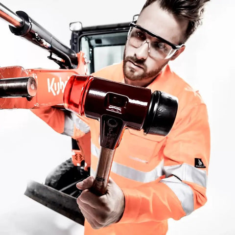 Person using Soft Face Mallet Workhorse with Dual Inserts, black rubber and red plastic, cast iron housing on a construction site