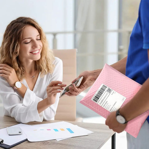 Person handing Light Pink Bubble Mailers 8.5x12 Inch 25 Pack Padded Envelopes to a seated woman.