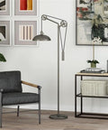 Spoke Wheel Pulley Floor Lamp With Metal Shade In Aged Steel Finish next to chair and artwork, industrial decor