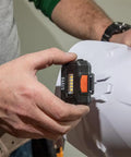Person attaching Rechargeable LED Headlamp with Adjustable Fabric Strap and Marker Holder to hard hat for work use.