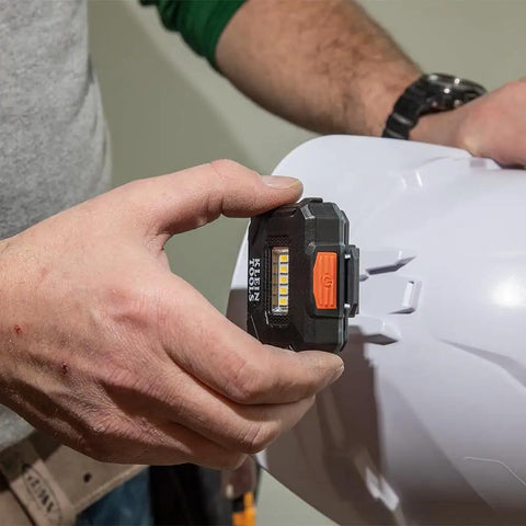 Person attaching Rechargeable LED Headlamp with Adjustable Fabric Strap and Marker Holder to hard hat for work use.